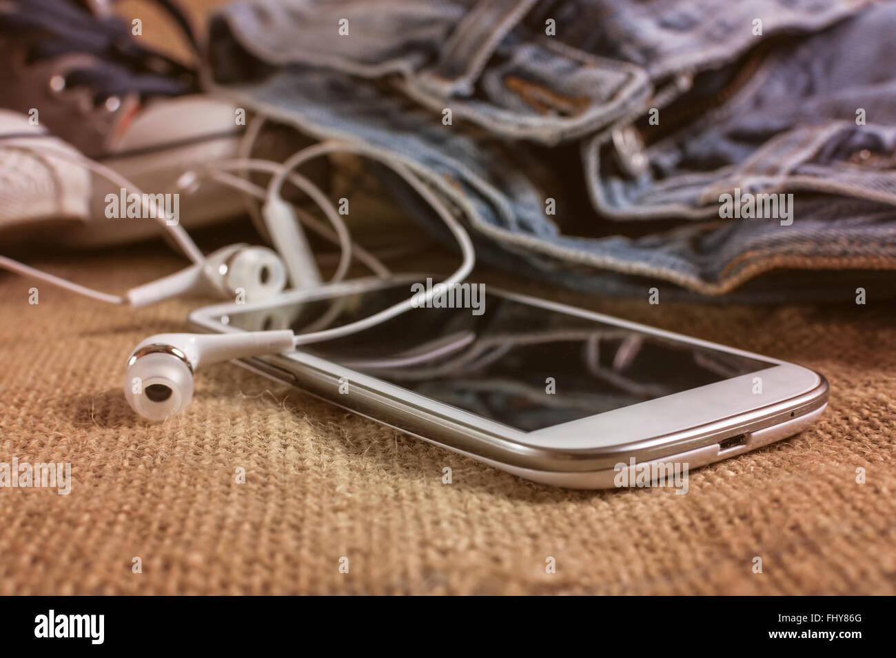 Smart phone on a table cloth with pants and sneakers. Shallow depth of field. Stock Photo