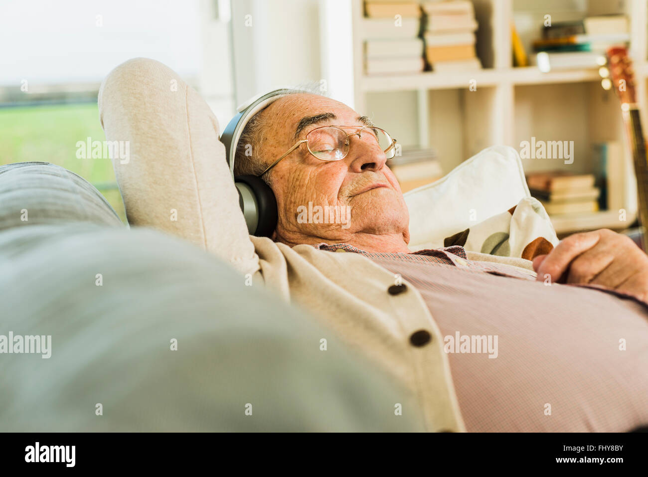 Senior man lying on the couch hearing music with headphones Stock Photo