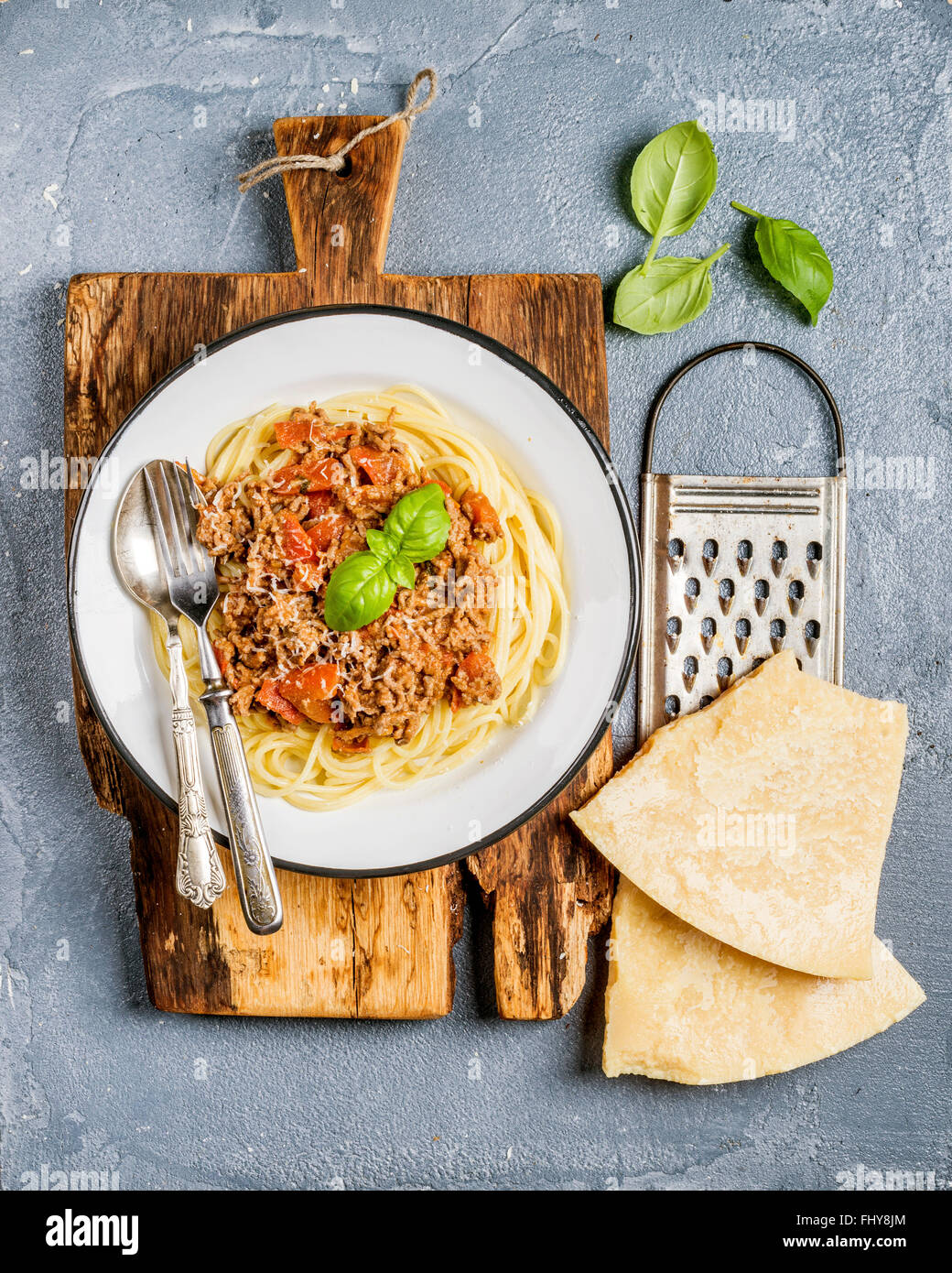 Pasta dinner. Spaghetti Bolognese in metal plate on rustic wooden board with Parmesan cheese grater and fresh basil on grey con Stock Photo