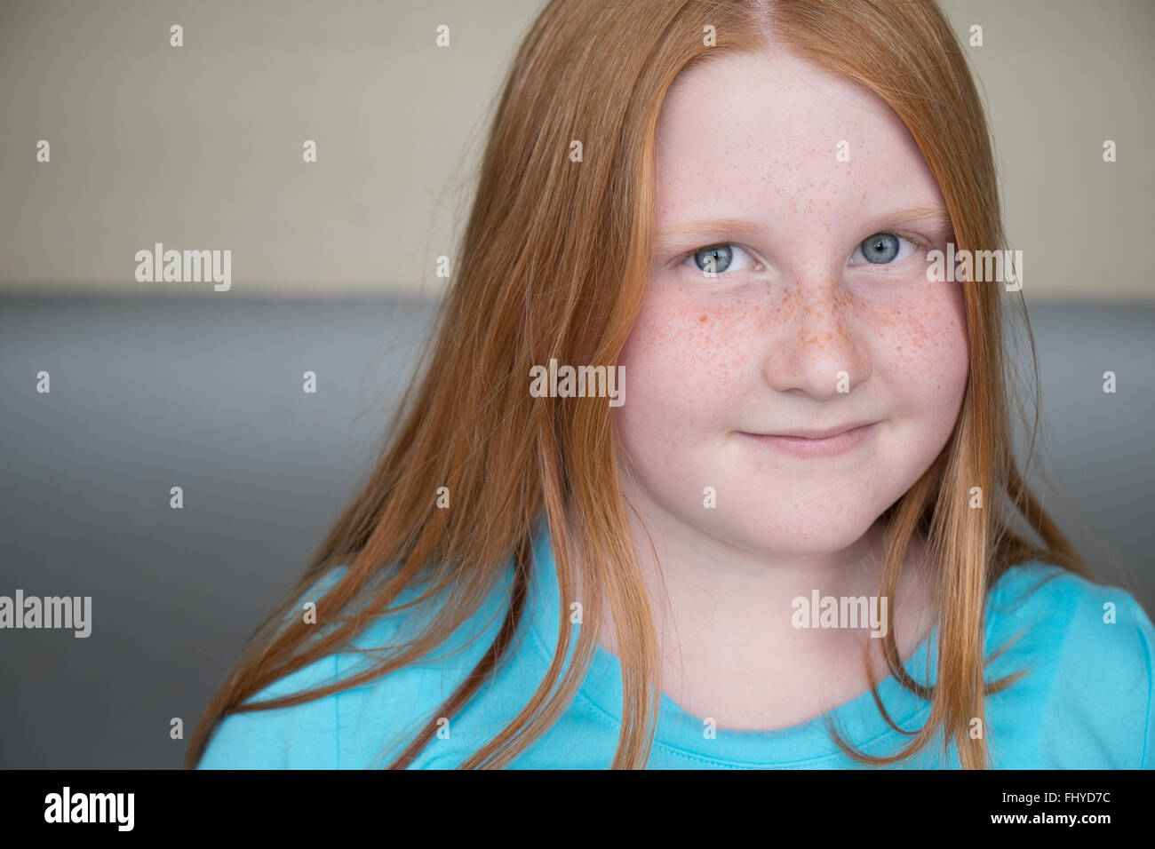 Red Haired, blue eyed Girl with a slight smile wearing a Blue Shirt close up looking at the camera Stock Photo