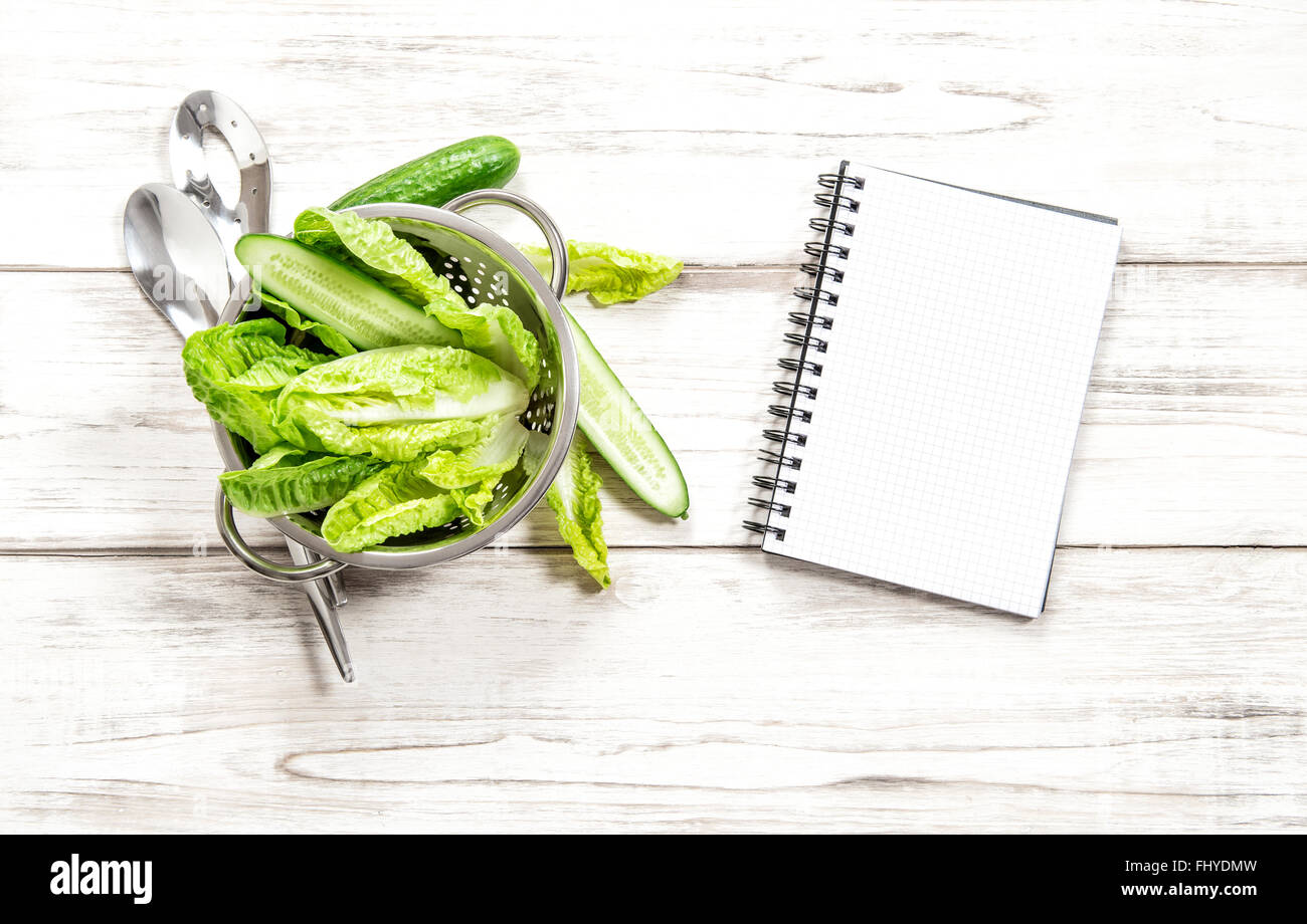 Green salad and vegetables with recipe book on kitchen table. Fresh food concept Stock Photo