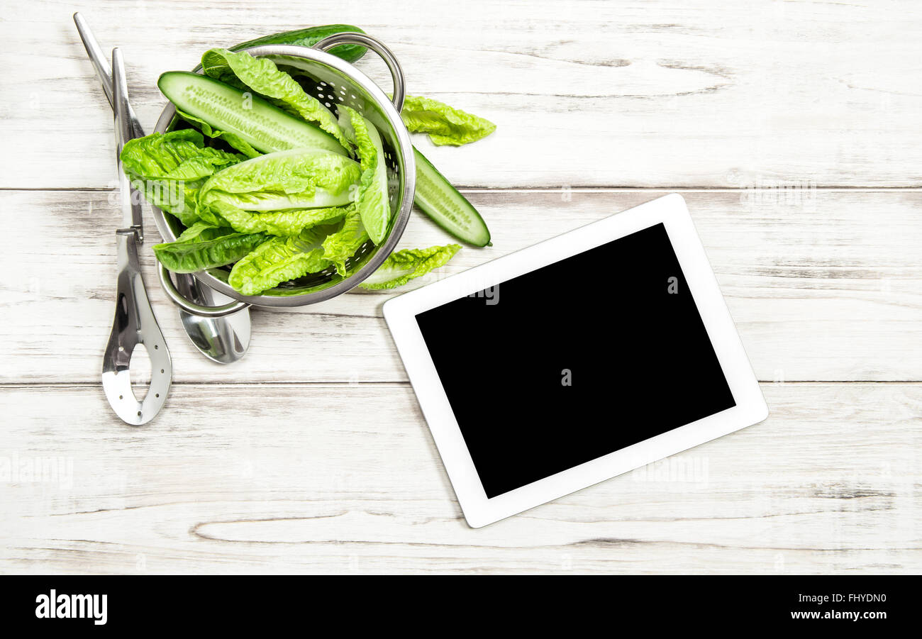Green salad vegetables with tablet pc on kitchen table. Internet online recipe book concept Stock Photo
