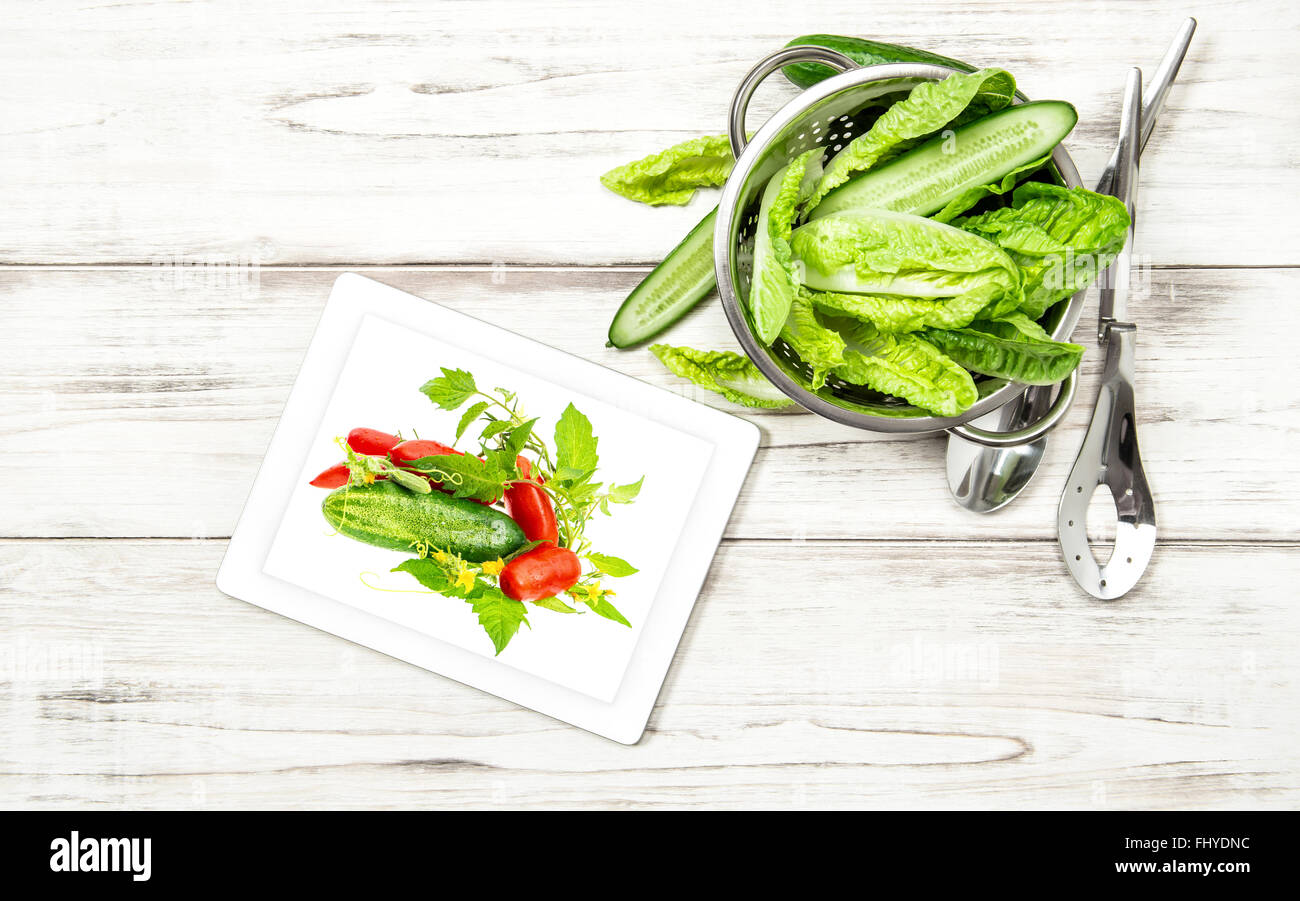 Green salad vegetables with recipe book tablet pc on kitchen table. Internet cook book concept Stock Photo