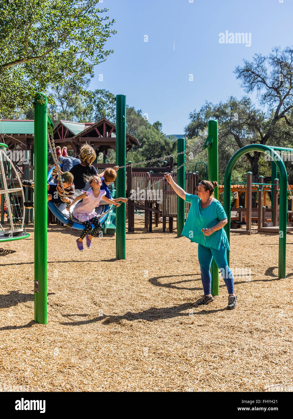 Four young kids having fun on a giant swing set that an adult female is swinging them on in Libbey Park, Ojai, California. Stock Photo