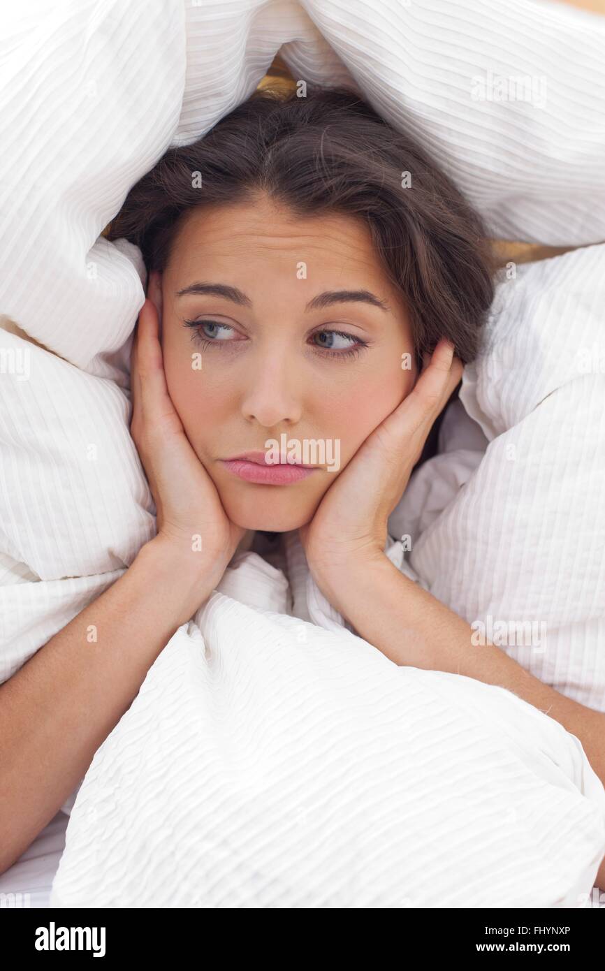 MODEL RELEASED. Woman in bed under the bedclothes with her hands on her chin. Stock Photo