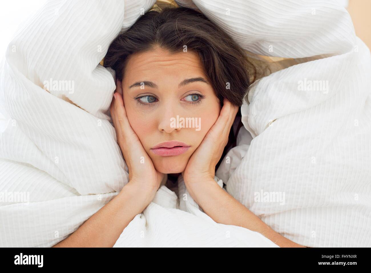 MODEL RELEASED. Woman in bed under the bedclothes with her hands on her chin. Stock Photo