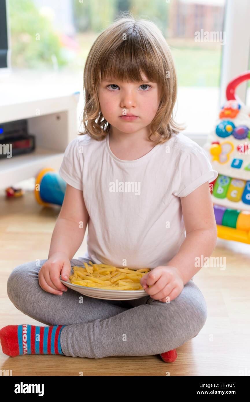 MODEL RELEASED. Young girl sitting on the floor with a plate of french fries. Stock Photo