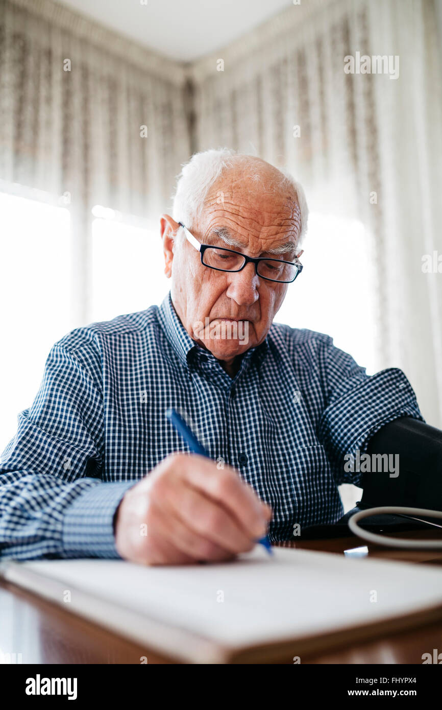 Senior man controlling his blood pressure and writing down the result Stock Photo