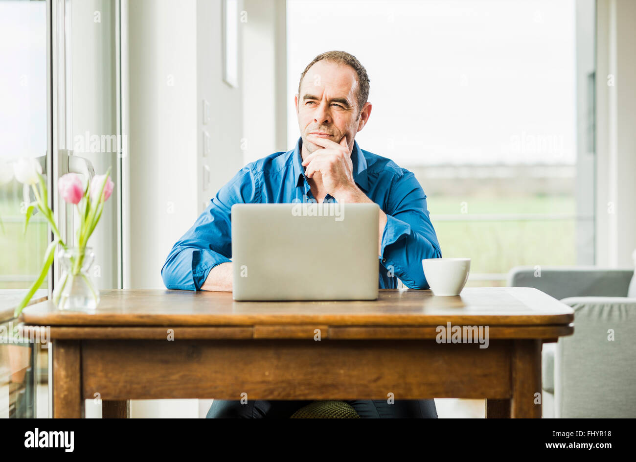 Businessman at home with laptop at wooden table thinking Stock Photo
