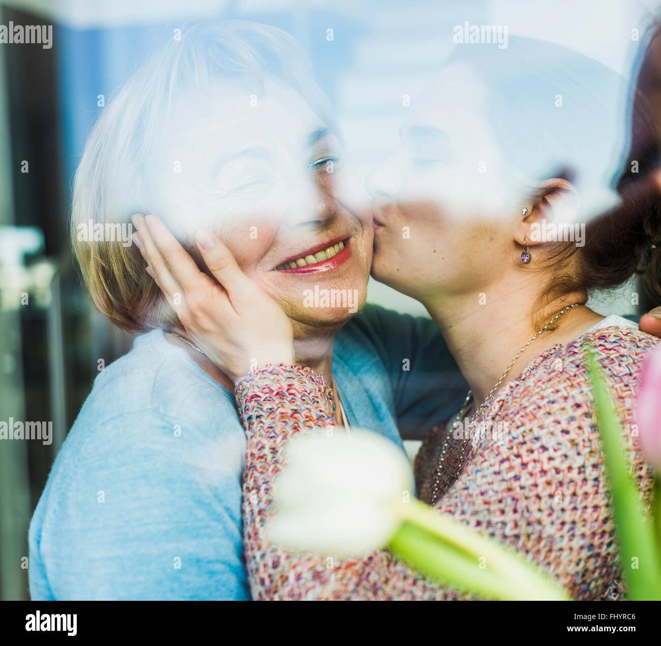 Young woman kissing senior woman behind windowpane Stock Photo