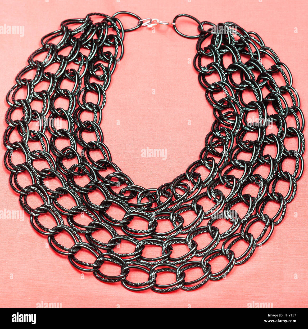 top view of necklace from strings of black chain on pink textile background Stock Photo