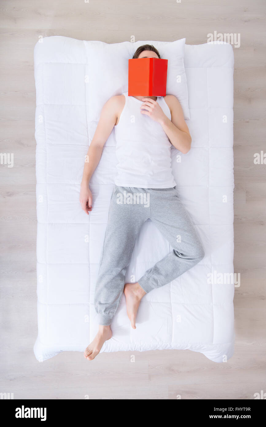 Sleeping man lying in bed with book Stock Photo