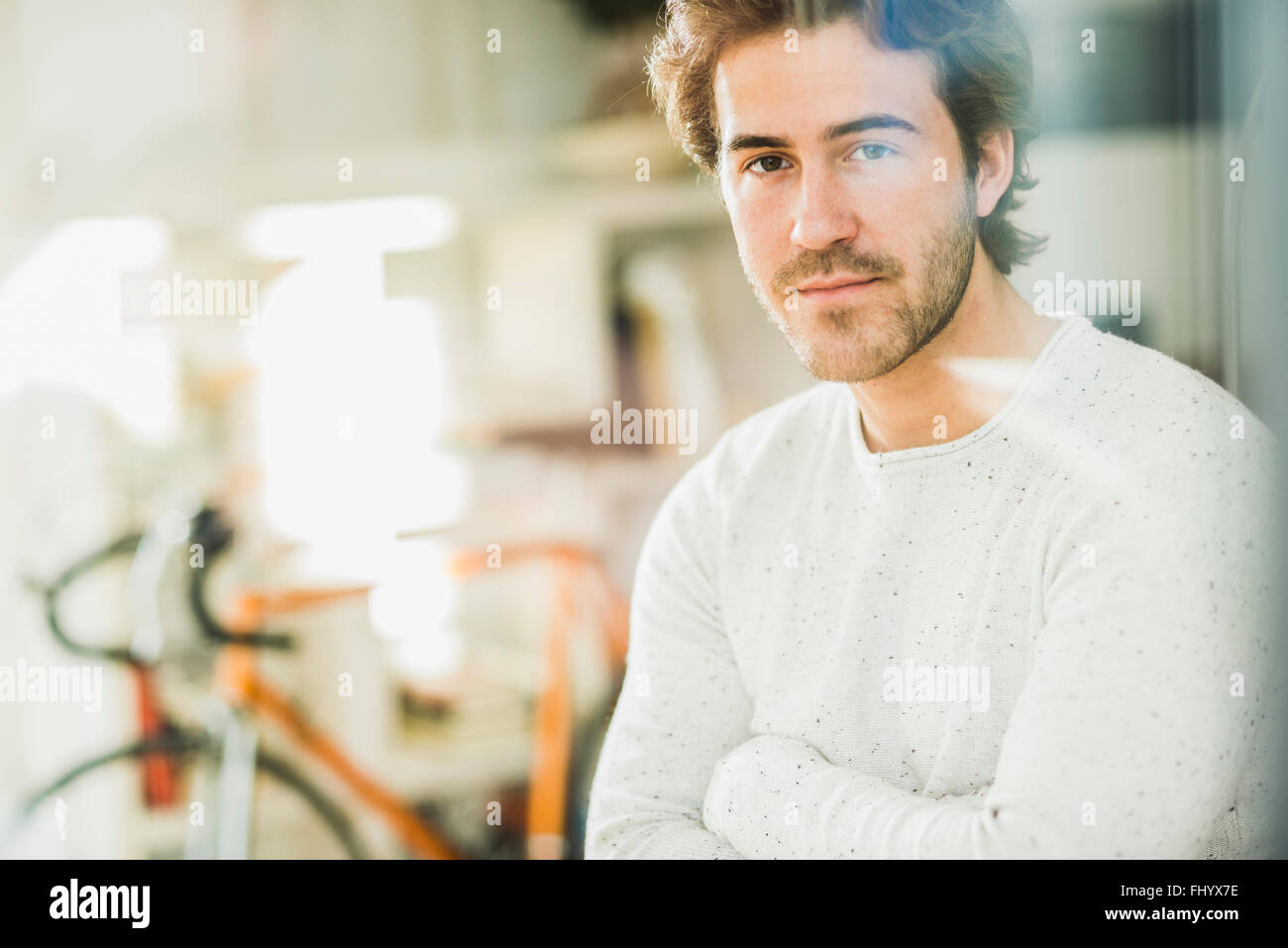 Portrait of young manwith arms crossed looking through windowpane Stock Photo