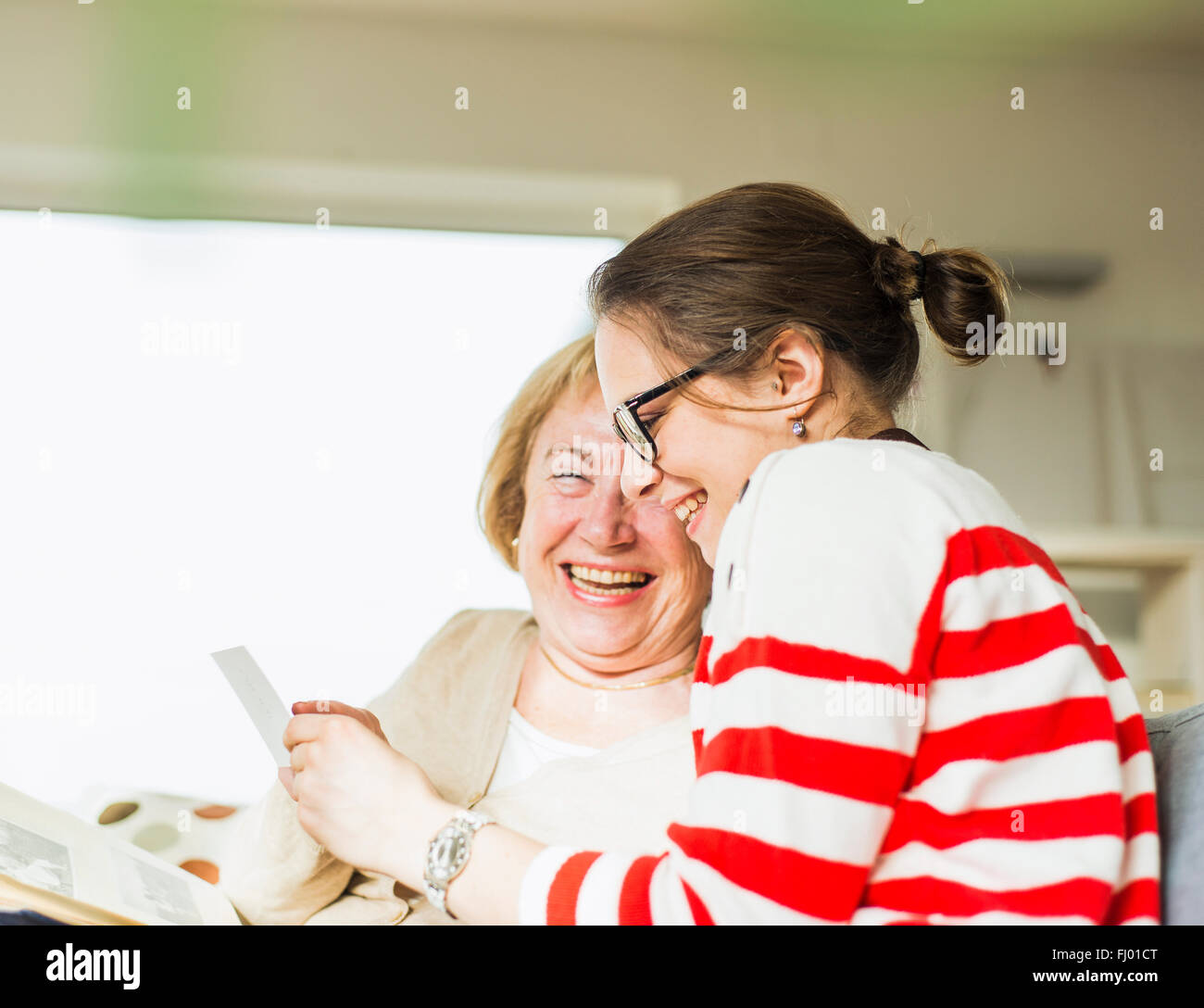 Happy senior woman and young woman sitting on couch looking at photo album Stock Photo