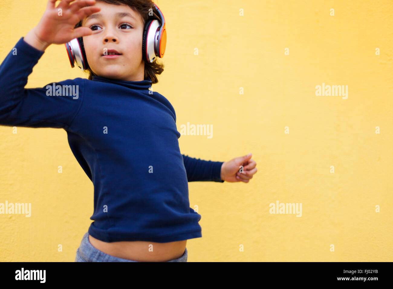 Dancing little boy in front of yellow wall hearing music with