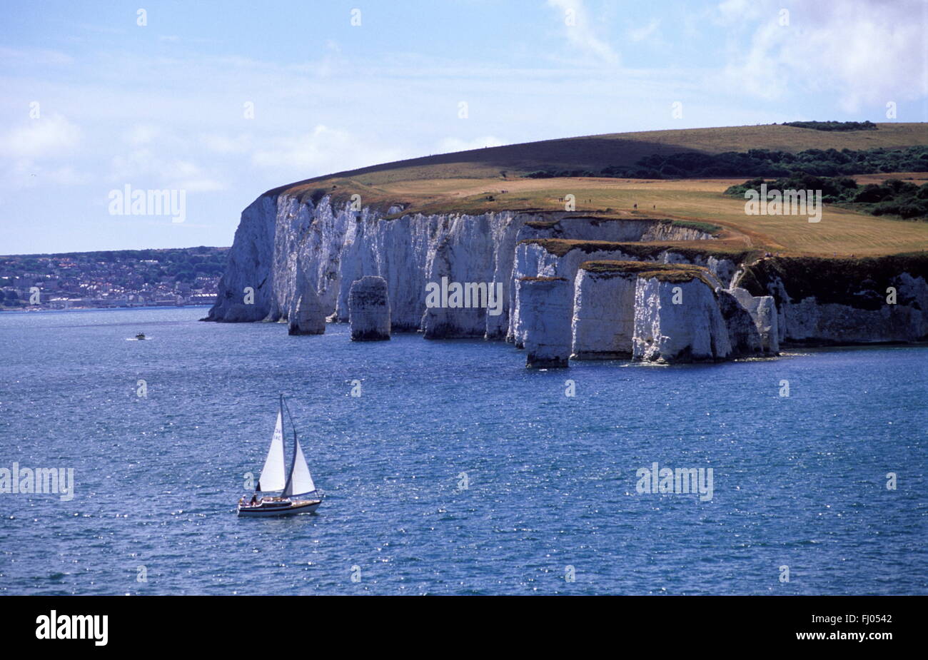Distinctive white cliffs of Studland  set in a blue sea. A small yacht with white sails rounds the point Stock Photo