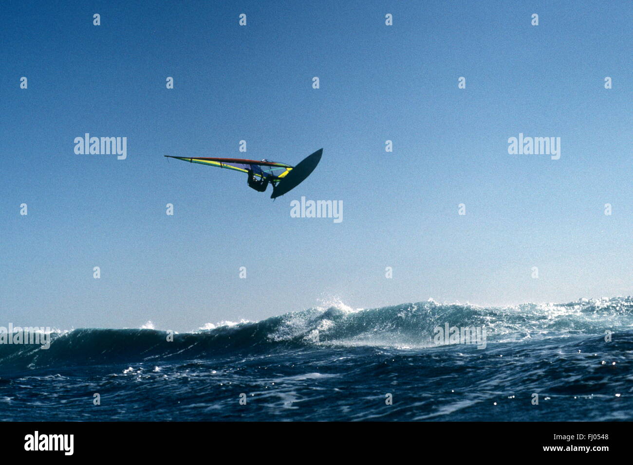 Jump of joy . Windsurfer leaps high over the waves against a clear blue