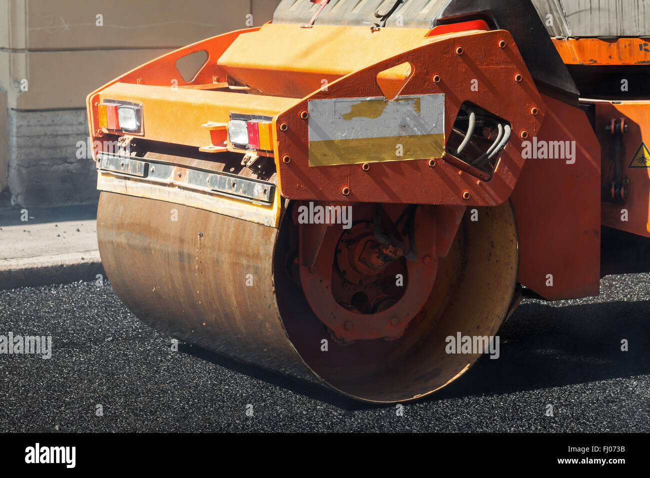 Fragment of orange roller, urban road is under construction, asphalting in progress Stock Photo