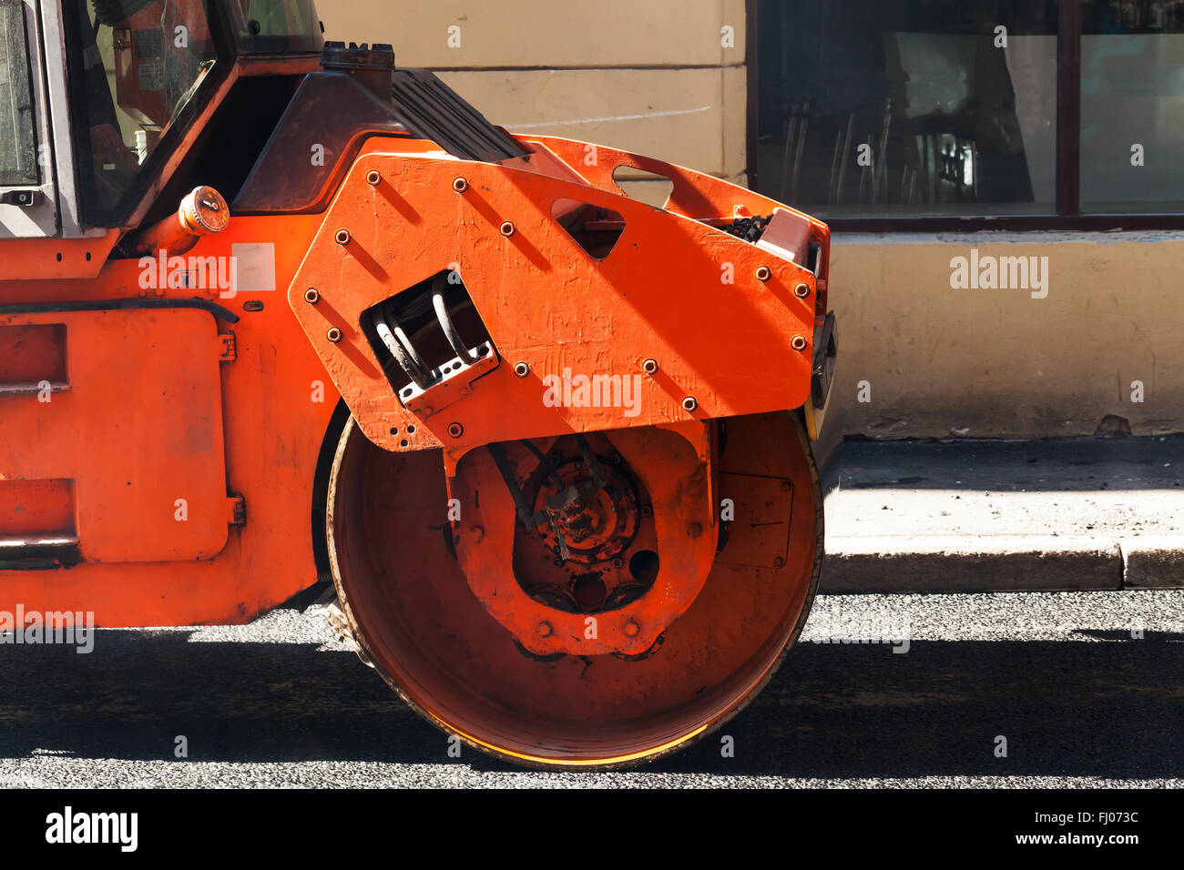Fragment of orange roller, urban road is under construction, asphalting in progress Stock Photo