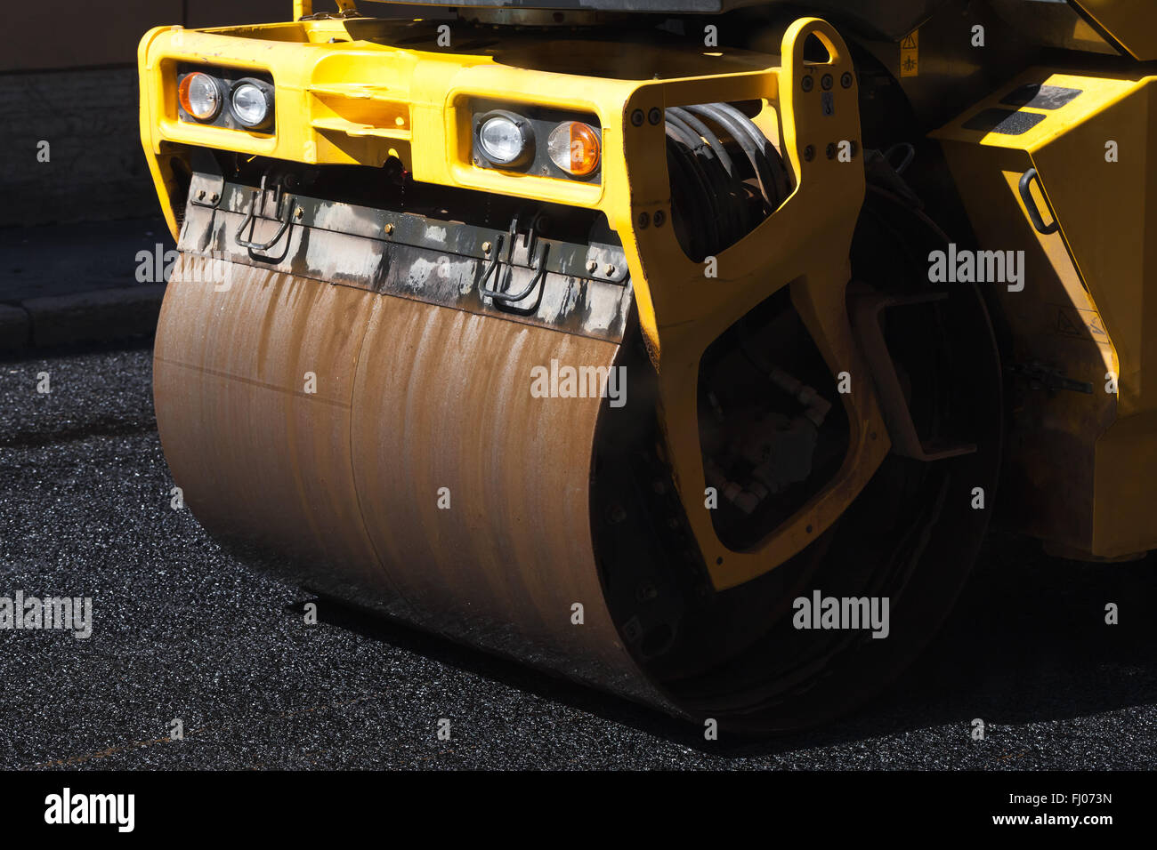 Fragment of yellow roller, urban road is under construction, asphalting in progress Stock Photo