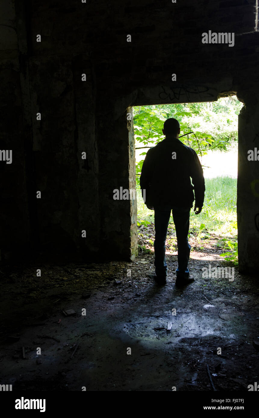 Mysterious male figure standing at the door of a derelict building