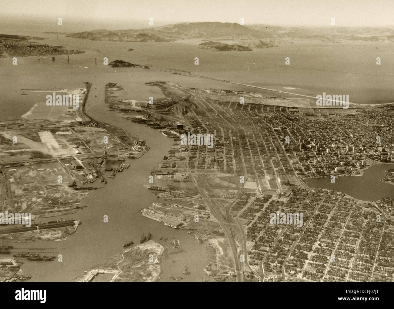 historical aerial photograph of Oakland, Alameda, Port of Oakland with Bay Bridge and Golden Gate Bridge under construction, California, 1935 Stock Photo