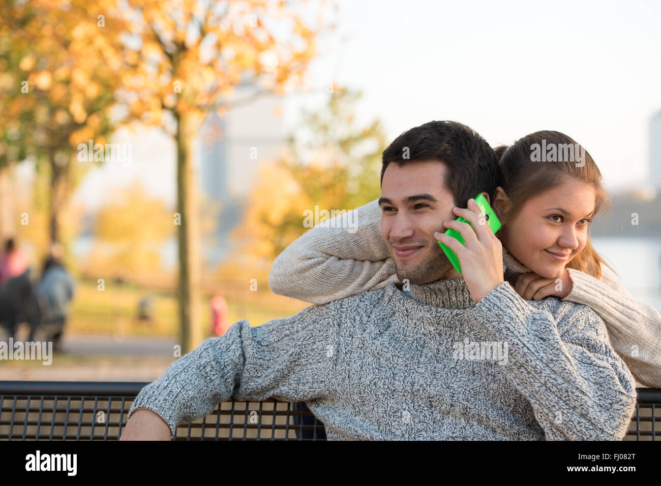 young couple in park sitting on bench, man is speaking on the smart ...