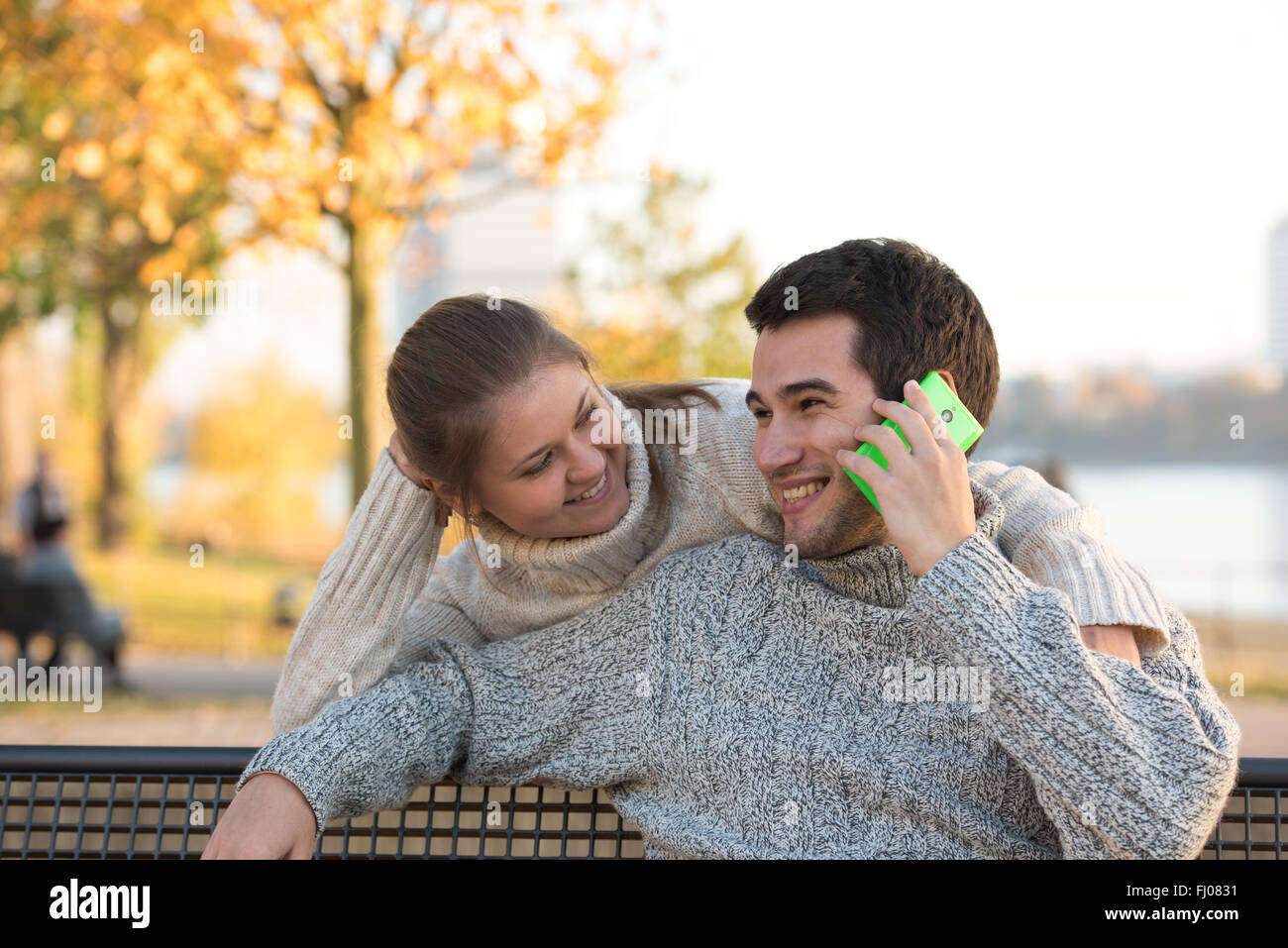 young couple in park sitting on bench, man is speaking on the smart ...