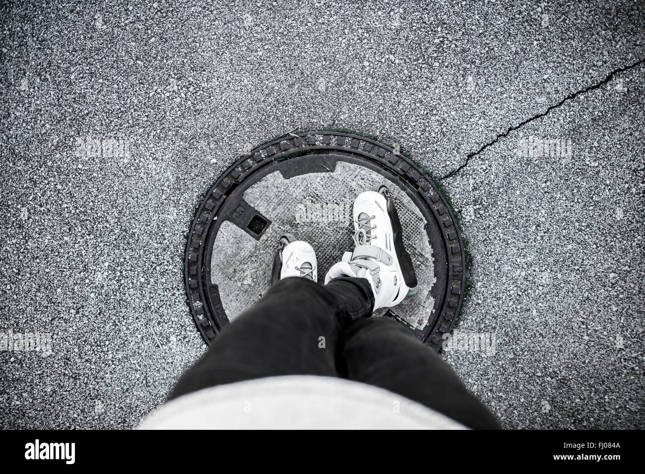 Young man with inline skates standing on manhole cover Stock Photo