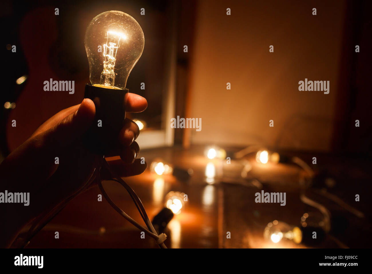 Incandescent light bulb, warm turned on. Garland of tungsten lamps. Light in darkness, copy space. Stock Photo