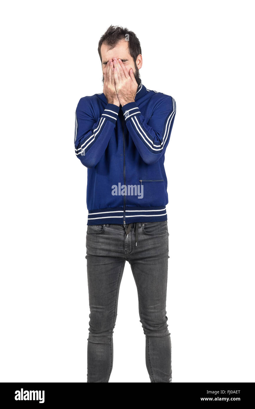 Bearded young man covering face with his hands laughing. Standing portrait isolated over white studio background. Stock Photo