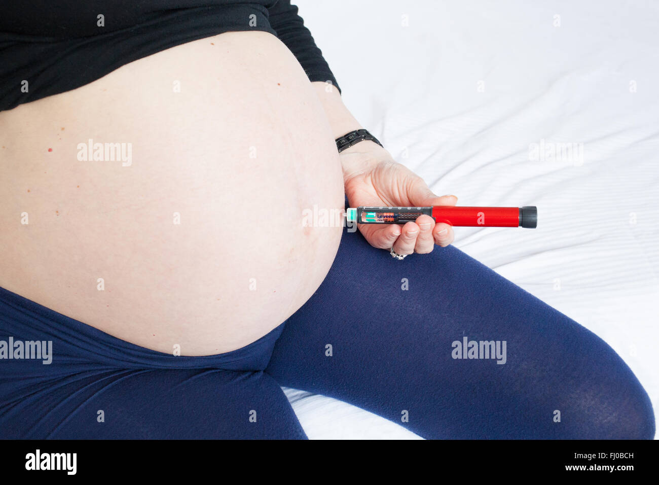 A nine month pregnant woman injects herself with the slow acting background insulin Levemir to control her Type 1 diabetes. Stock Photo
