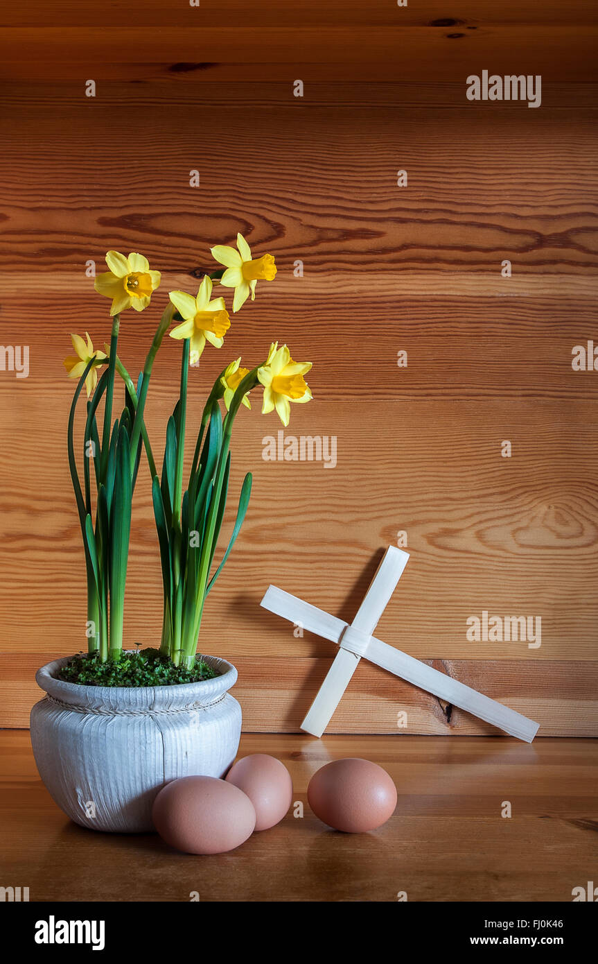 Pot of daffodils with palm cross and three eggs on pine wood. Stock Photo