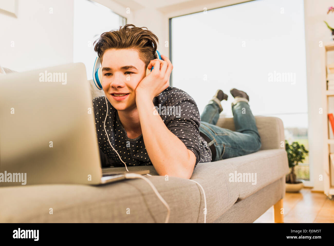 Young man lying on couch using laptop and headphones Stock Photo