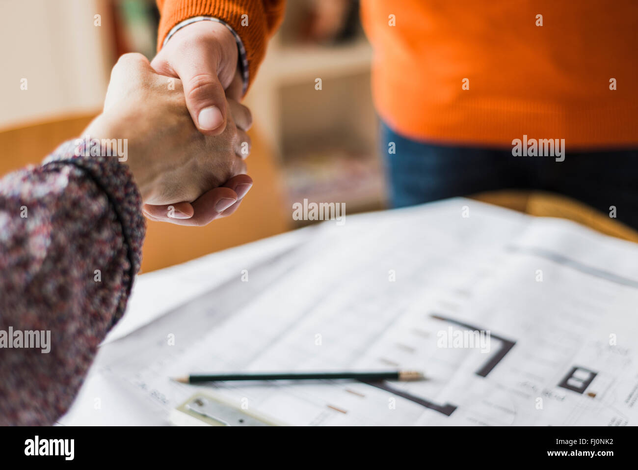 Close-up of man and woman shaking hands above plan Stock Photo