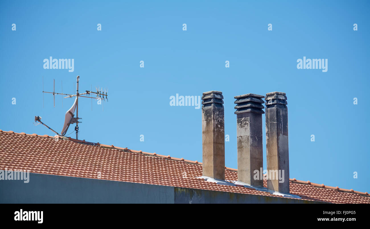 three chimneys and an old antennas on a tile roof Stock Photo