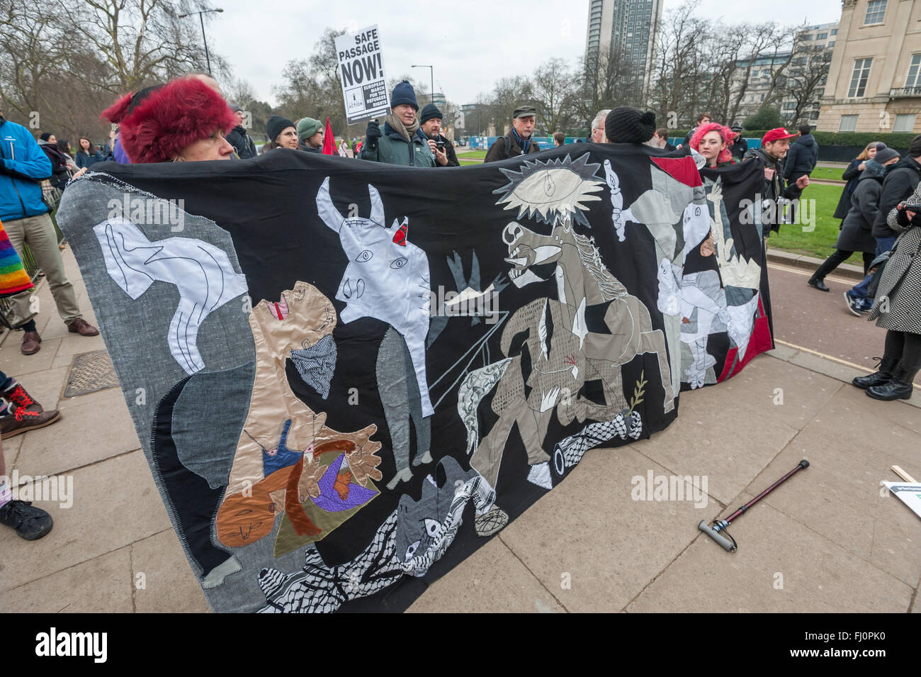 London, UK. 27th February 2016. People at Hyde Park Corner hold a banner made by Brighton refugee support groups based on Picasso's Guernica for the march to a rally at Marble Arch on the same day as protests in other cities across Europe to demand that authorities and governments take action now to open secure safe passage routes for all refugees and asylum seekers seeking protection in Europe. They want an end to deaths at borders and for refugees to be allowed to keep their possessions and be reunited with their families. Peter Marshall, Alamy Live News Stock Photo