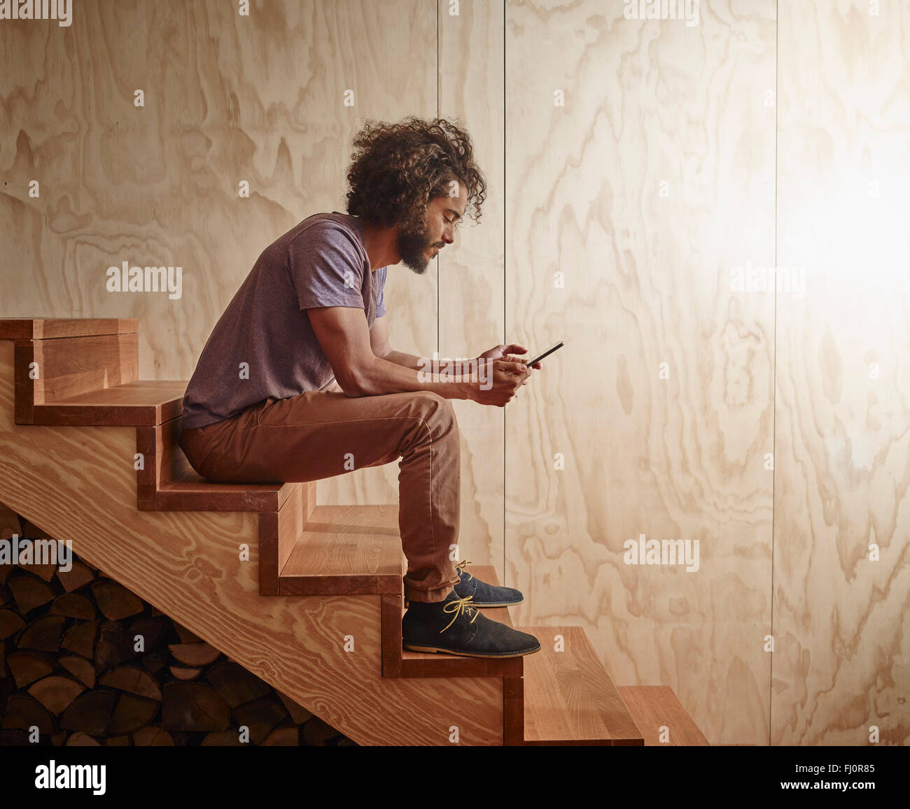 Young man sitting on wooden stairs looking at digital tablet Stock Photo