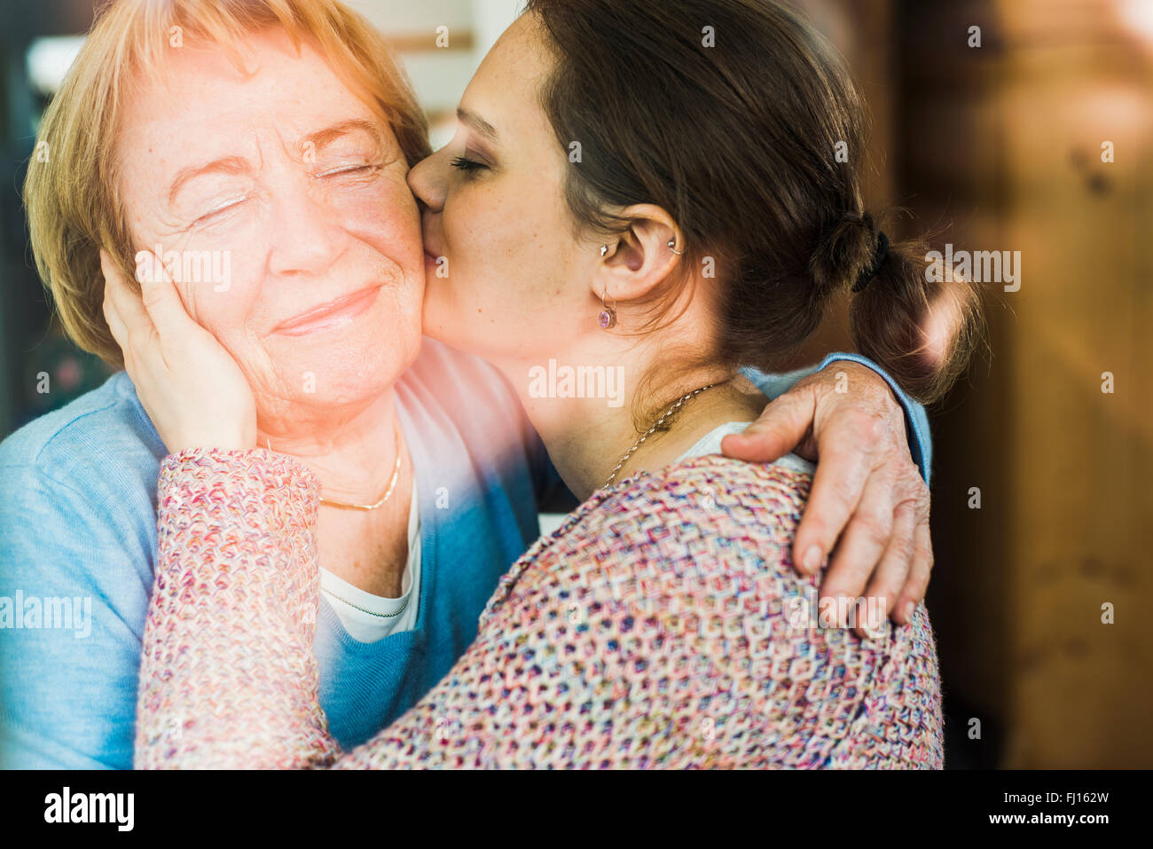 Young woman kissing senior woman behind windowpane Stock Photo