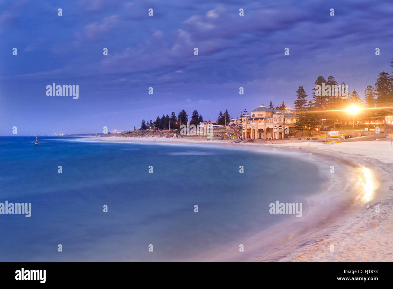 Perth western Indian ocean facing sandy beach Cottesloe at sunset. Central pavilion with lights and trees above blurred waves Stock Photo