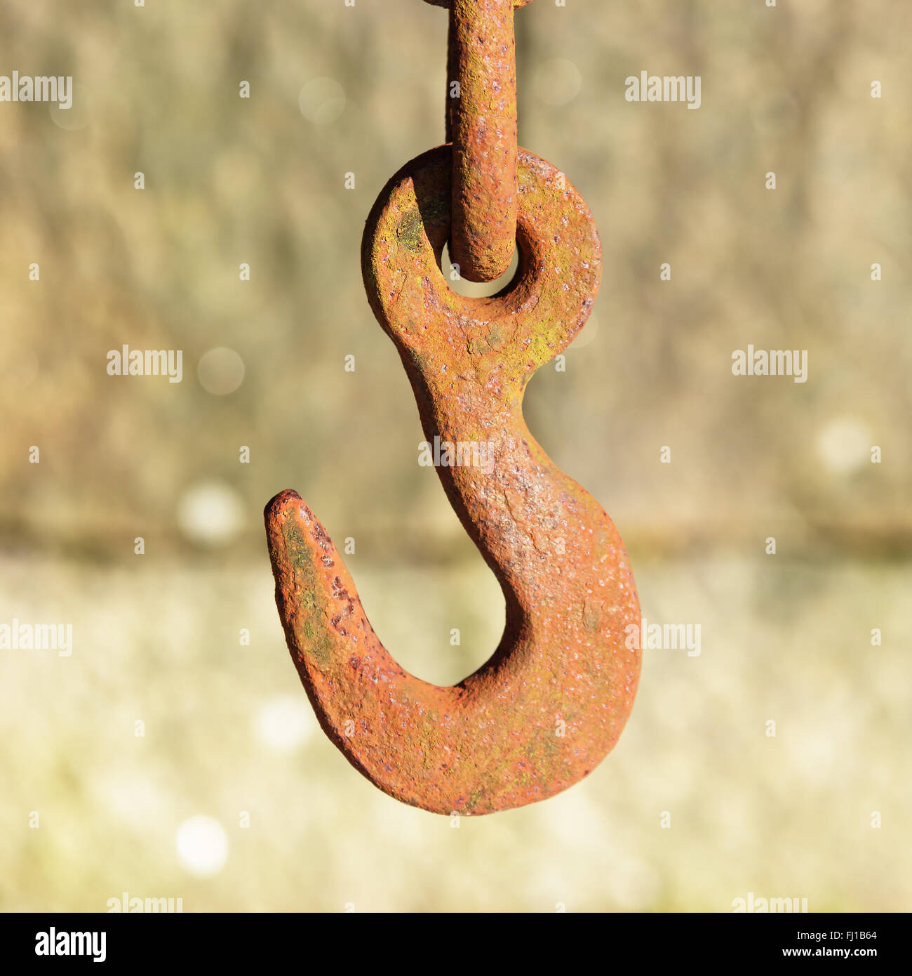 A rusty old steel hook hang down with blurred stone block in background