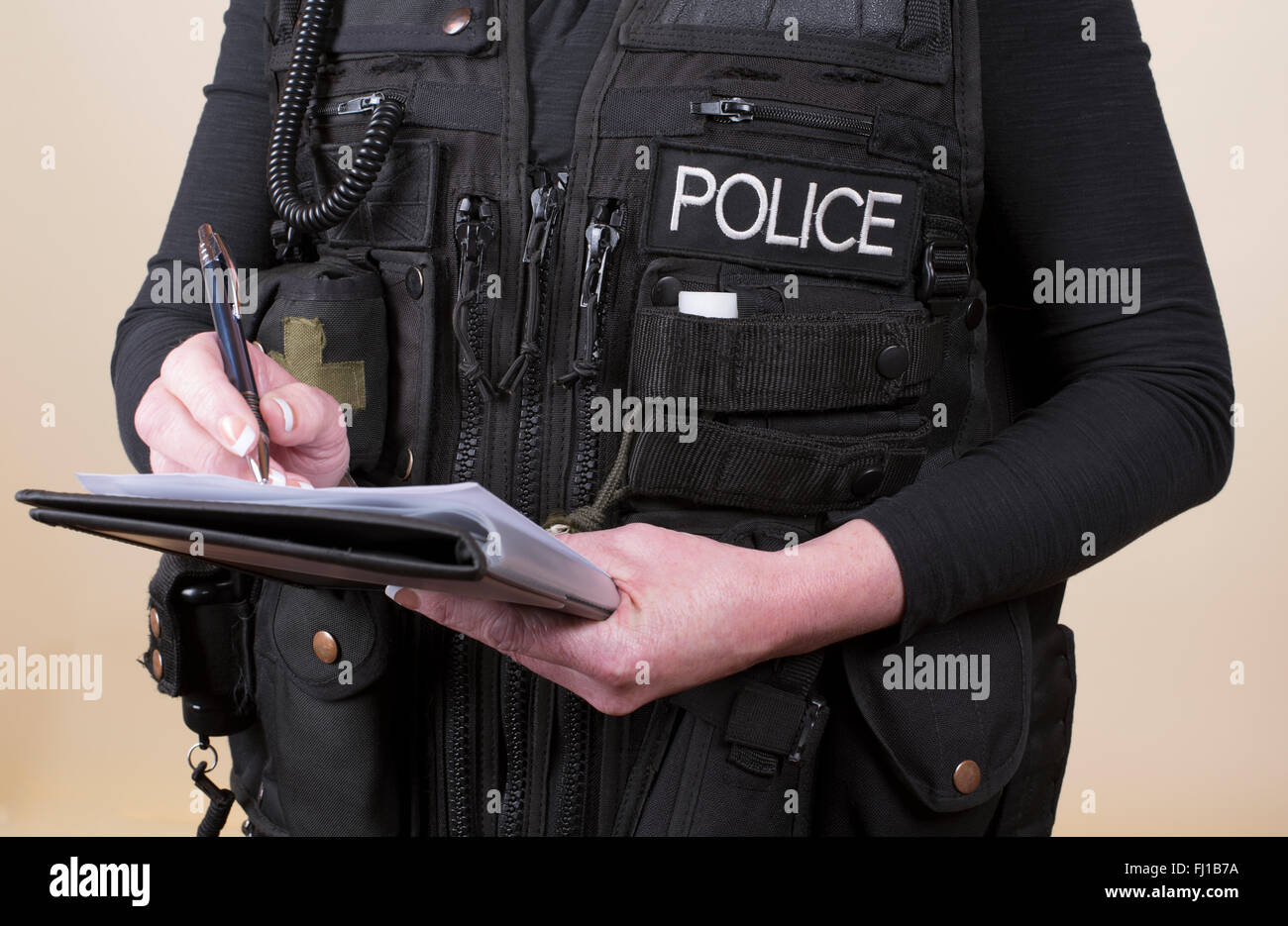 Police officer wearing tactical vest writing notes on a pad Stock Photo