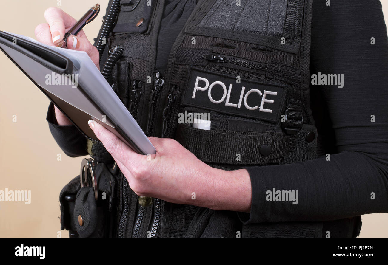 Police officer wearing tactical vest writing notes on a pad Stock Photo