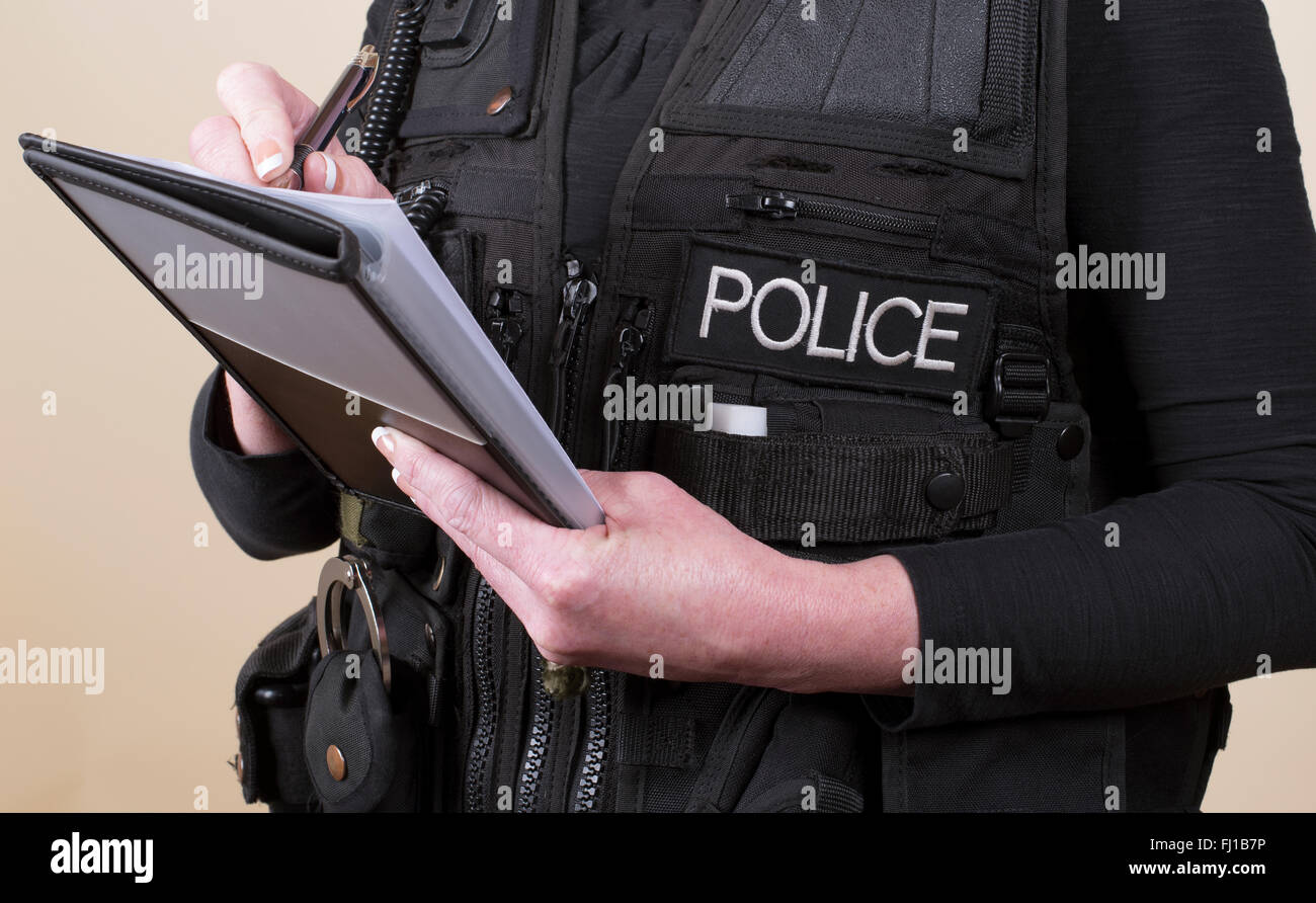 Police officer wearing tactical vest writing notes on a pad Stock Photo