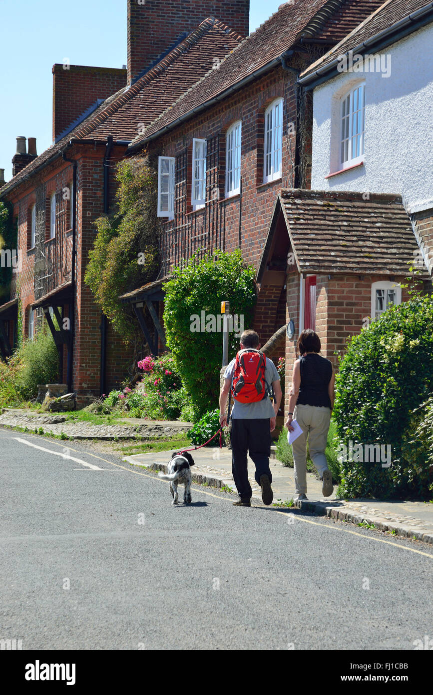 Rear view of adult man and woman walking with dog through the attractive village of Itchenor, Chichester Harbour, West Sussex, England, UK Stock Photo