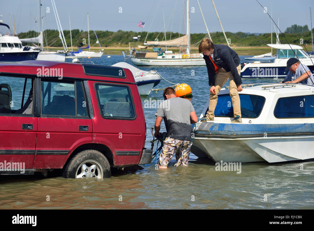 Boat on a road trailer being coupled to car's hitch to pull out of the water in Chichester Harbour at  Itchenor, Chichester, West Sussex, UK Stock Photo