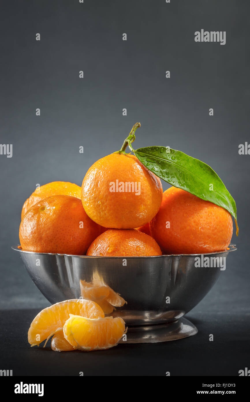 Clementines with leaf in metallic bowl on dark background Stock Photo