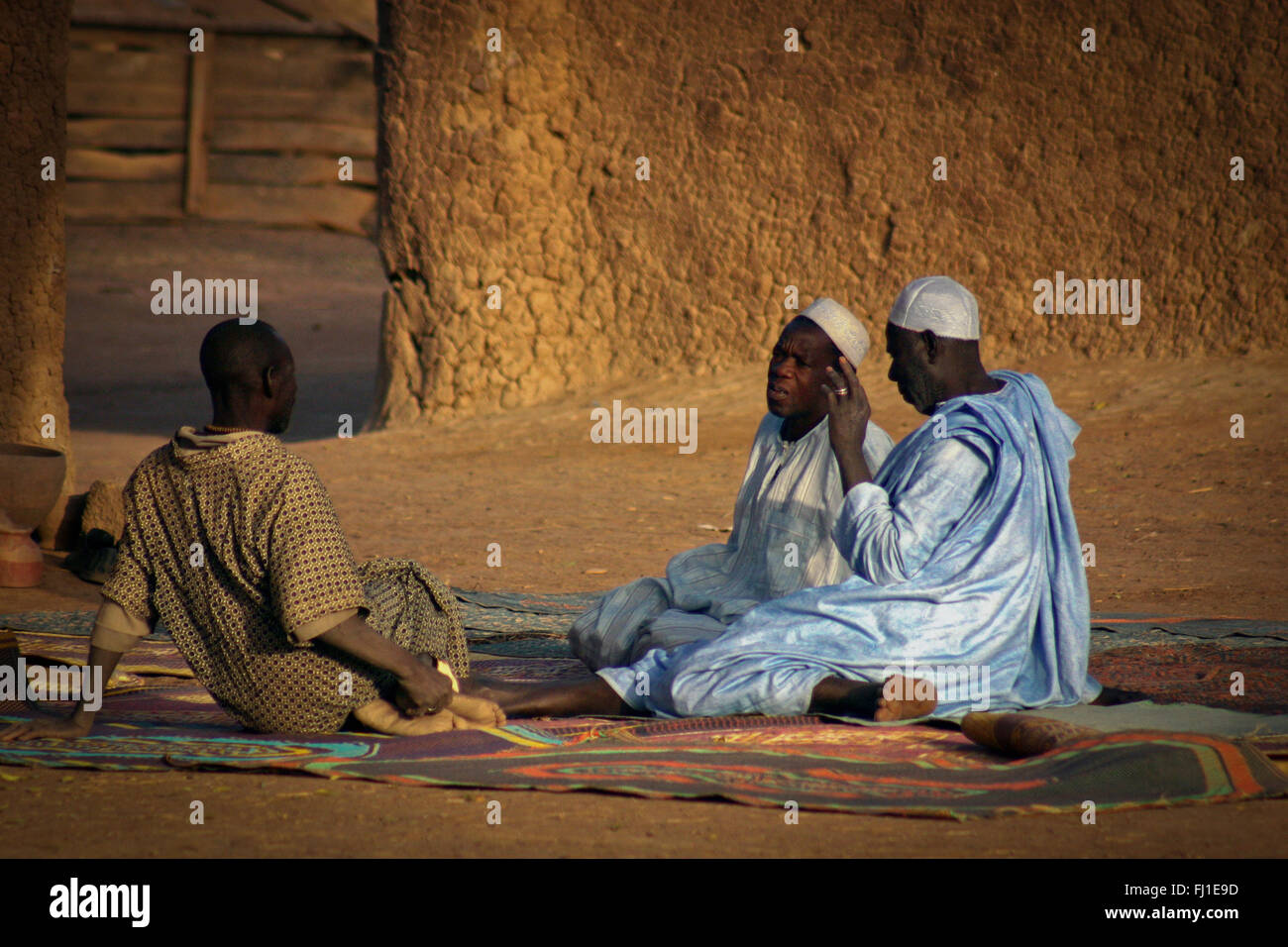 Three men are talking in Djenné , Mali, sitting on the ground in the early morning with traditional clothes Stock Photo