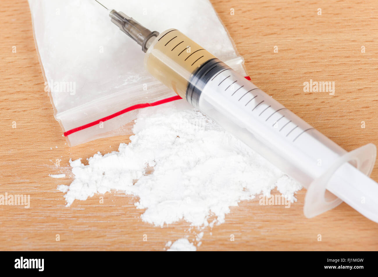 Loaded heroin syringe laying across a spilled bag of heroin on a table Stock Photo