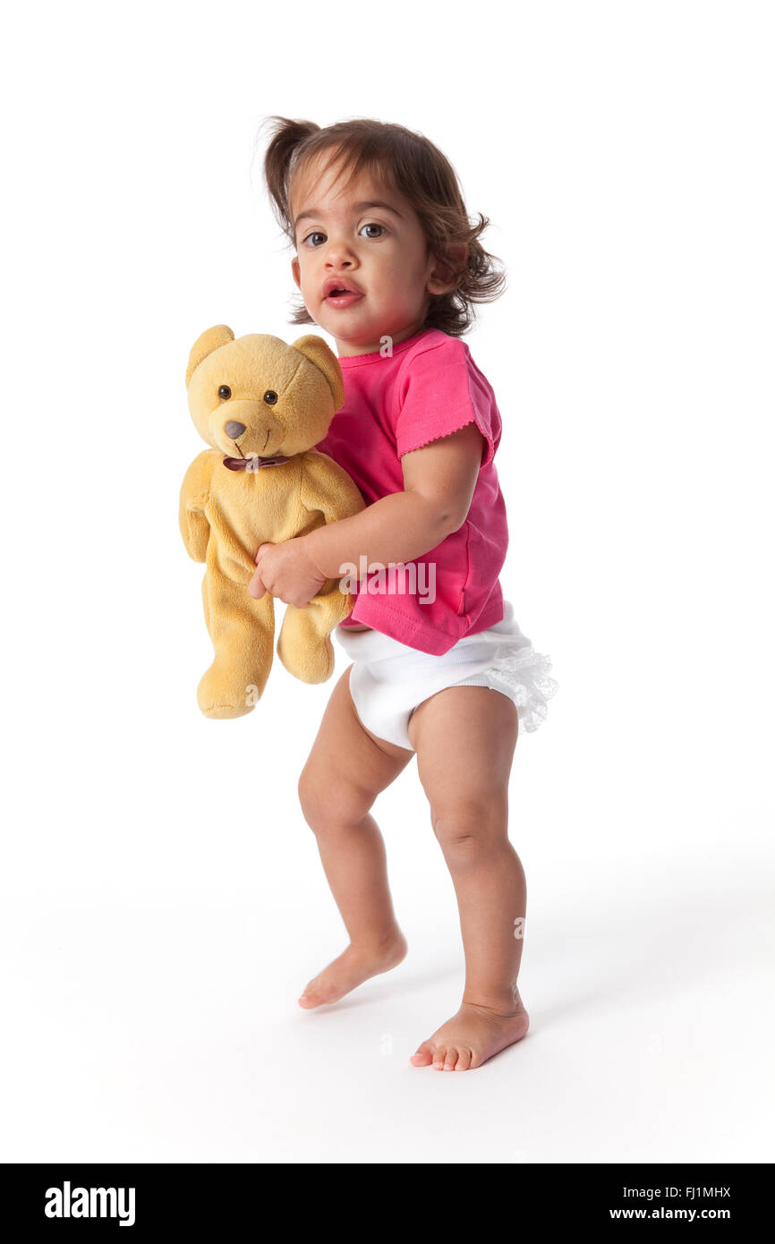 Baby girl walking with a toy bear on white background Stock Photo